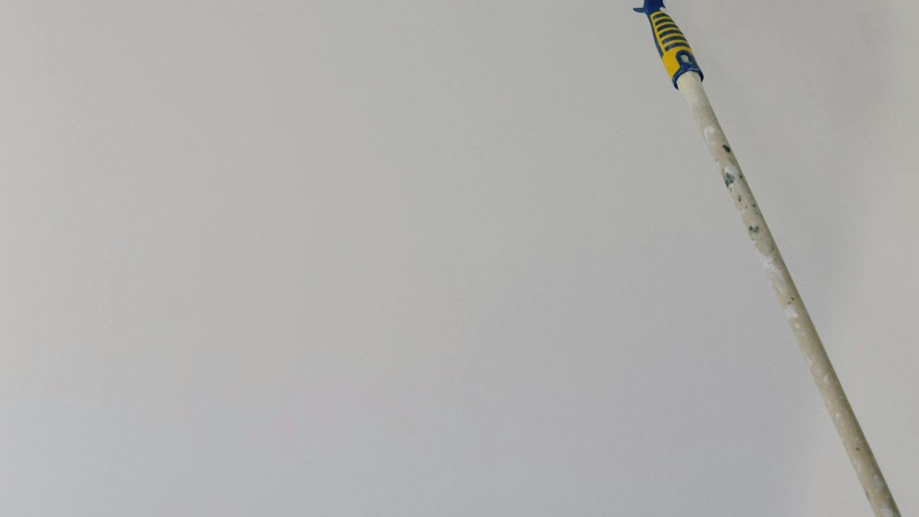 Paint roller with white acrylic paint on wall in room during renovation at home