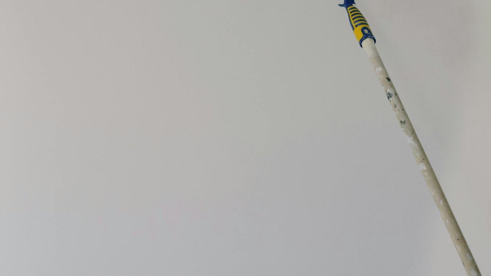 Paint roller with white acrylic paint on wall in room during renovation at home