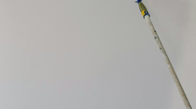 Paint roller with white acrylic paint on wall in room during renovation at home